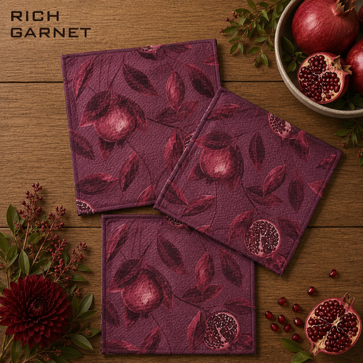 Geometry rich garnet square dishcloth set of three in a rich garnet purple color with a pomegranate and leaf pattern, arranged on a wooden table with pomegranate props and green leaves. The brand name 'RICH GARNET' is visible in the top left corner.  The Little Exchange SKU 150062