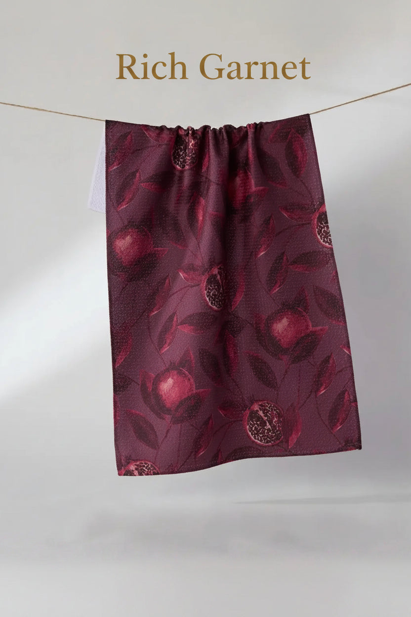A Geometry rich garnet tea towell with a pomegranate pattern, hanging from a thin wire against a plain light gray background.