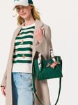 Woman holding an emerald green shiraleah danny mini handbag with decorative elements, wearing a striped shirt and beige coat.