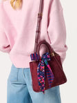 Person holding a wine colored Shiraleah Danny Mini Tote handbag with a colorful ribbon, wearing a pink sweater and blue jeans.