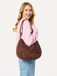 Woman holding a brown Shiraleah Danny brown shoulder handbag with a pink top.