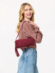 Woman wearing a pink sweater and jeans holding a Shiraleah Kylie shoulder bag in wine on a plain background