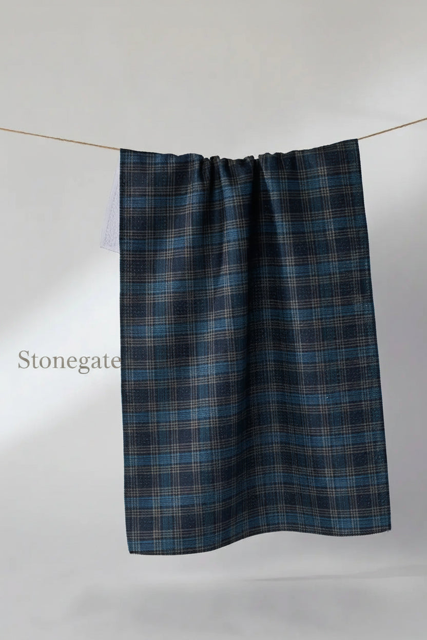 A dark blue and black plaid kitchen Geometry stonegate tea towel hanging from a thin wire against a light gray background.