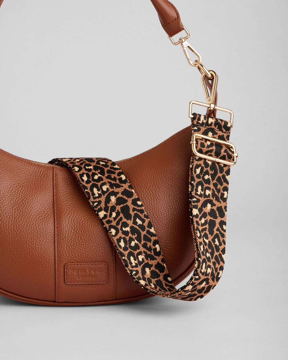 Brown leather handbag with a leopard print strap on a light gray background