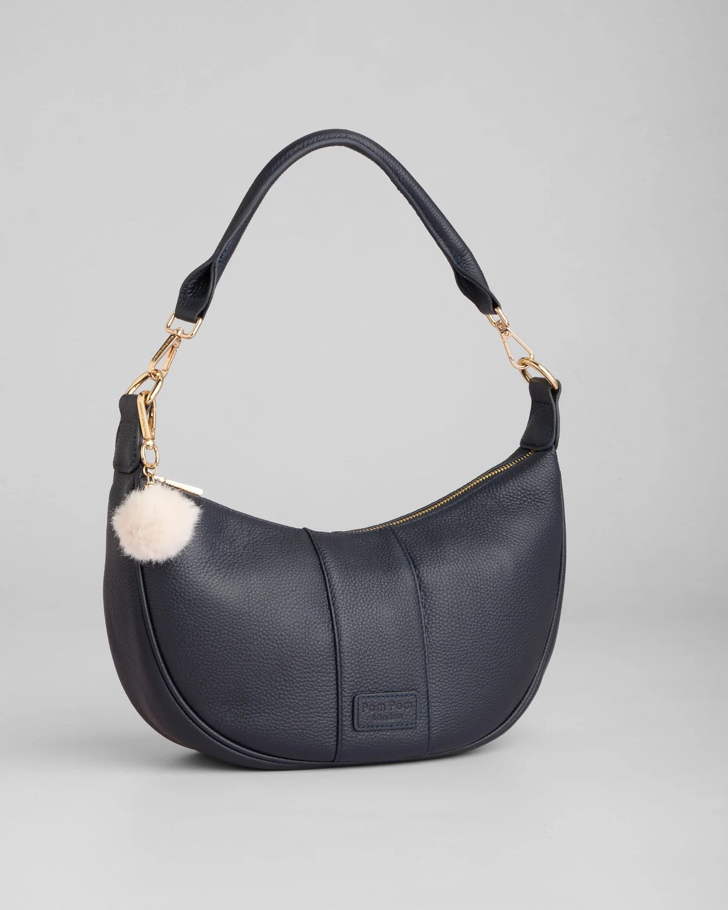 pom pom london sutton sling bag in a navy color with a cream pom pom tassel