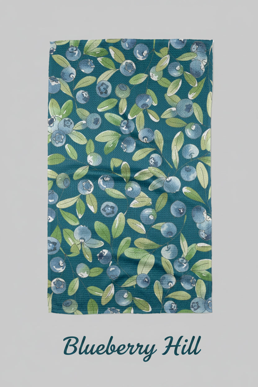 A blue Geometry Blueberry Hill kitchen tea towel with a geometric pattern featuring blueberries and green leaves.