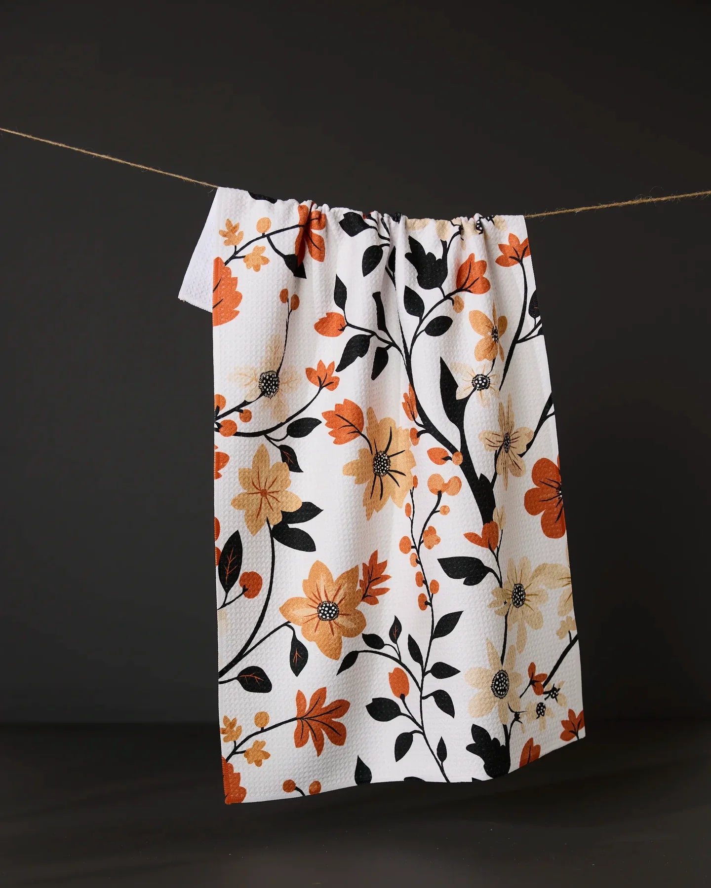 Floral patterned Geometry Spiced Florals tea towel hanging on a line against a black background
