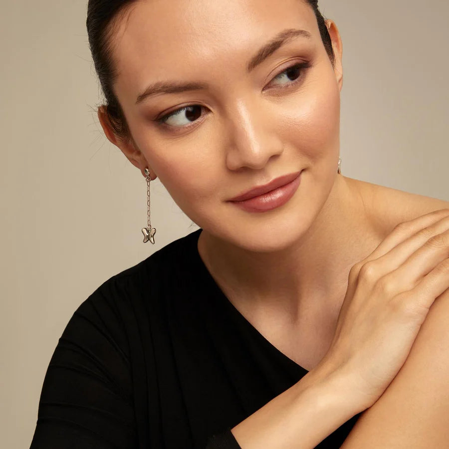 Woman wearing a silver dangle UNOde50 butterfly wings earring with a neutral background