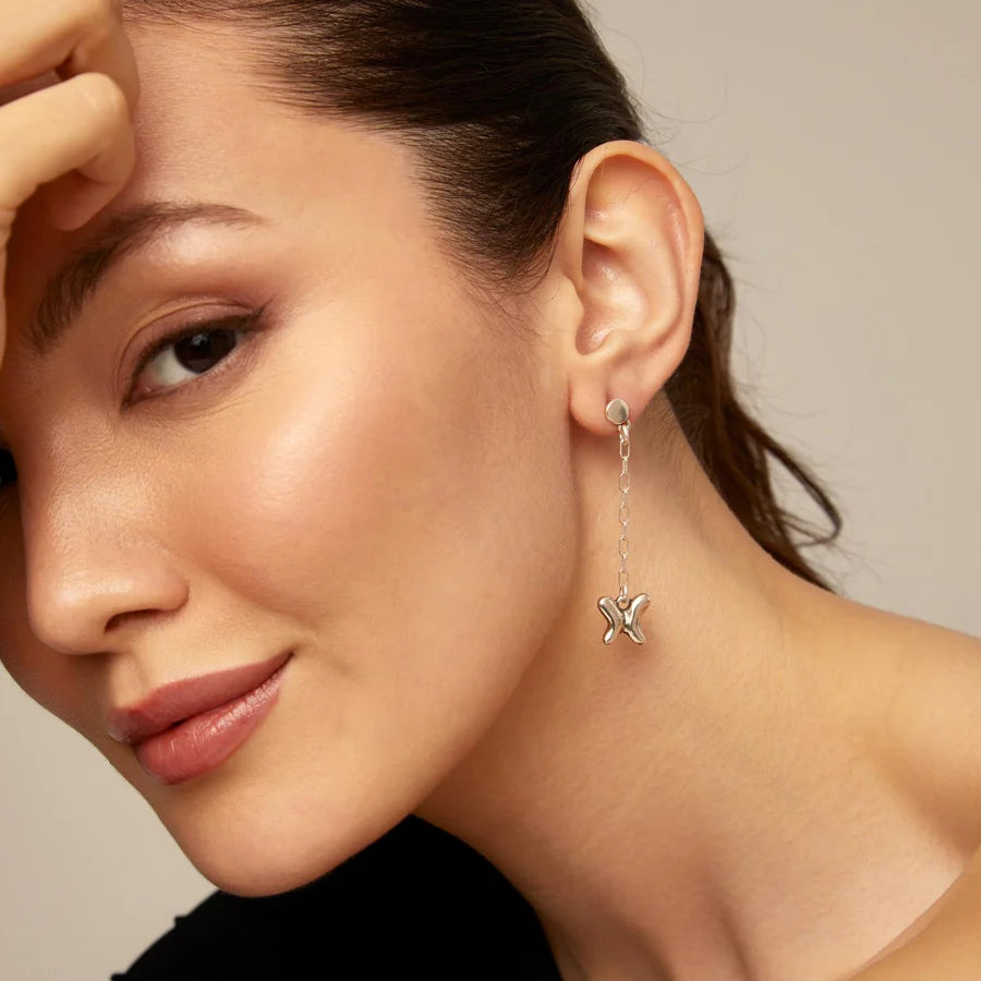 Close-up of a woman wearing UNOde50 Wings Silver Dangle Butterfly Earrings against a neutral background