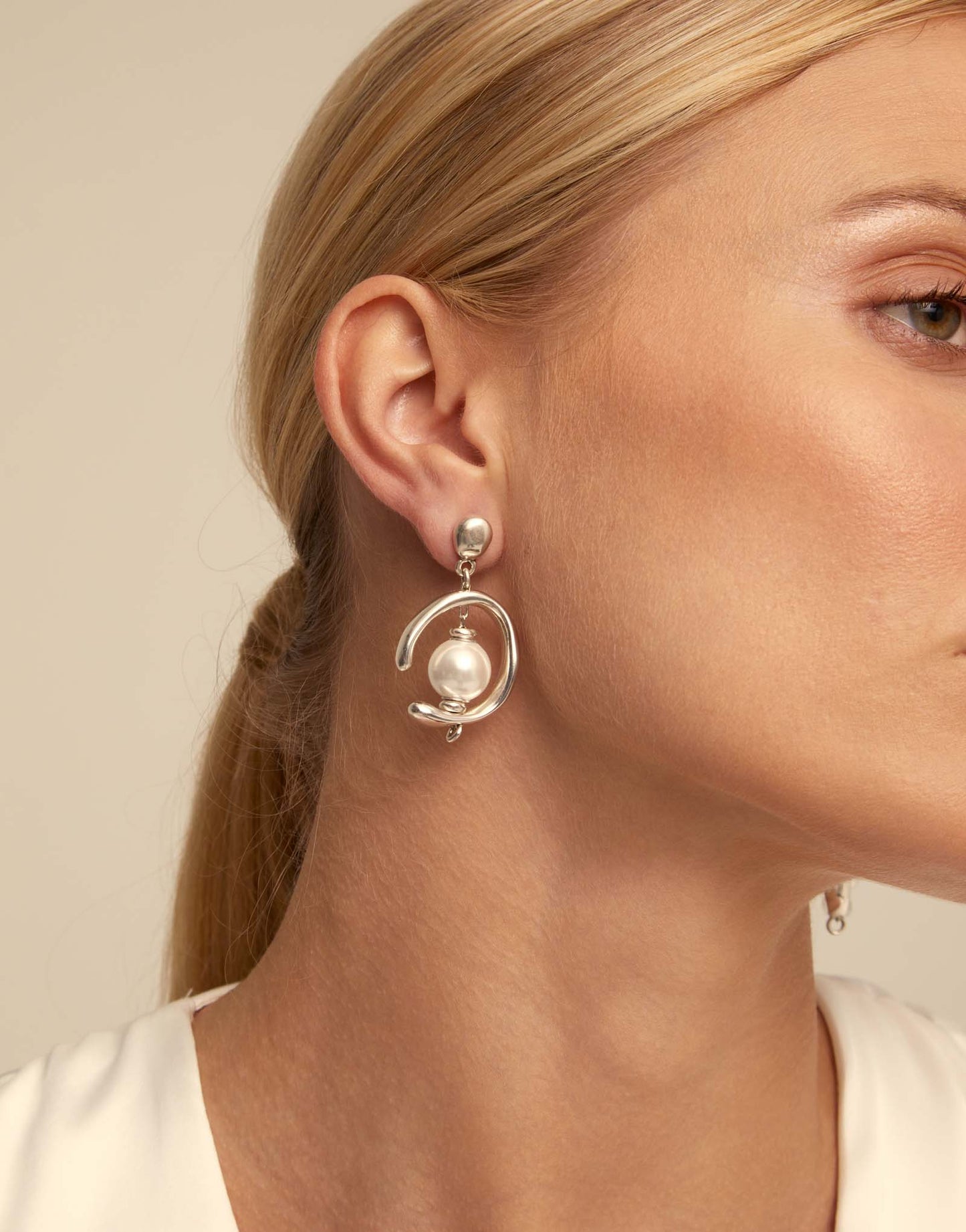 Close-up of a woman wearing UNOde50 Inorbit Silver Drop Earrings with Pearls on a beige background