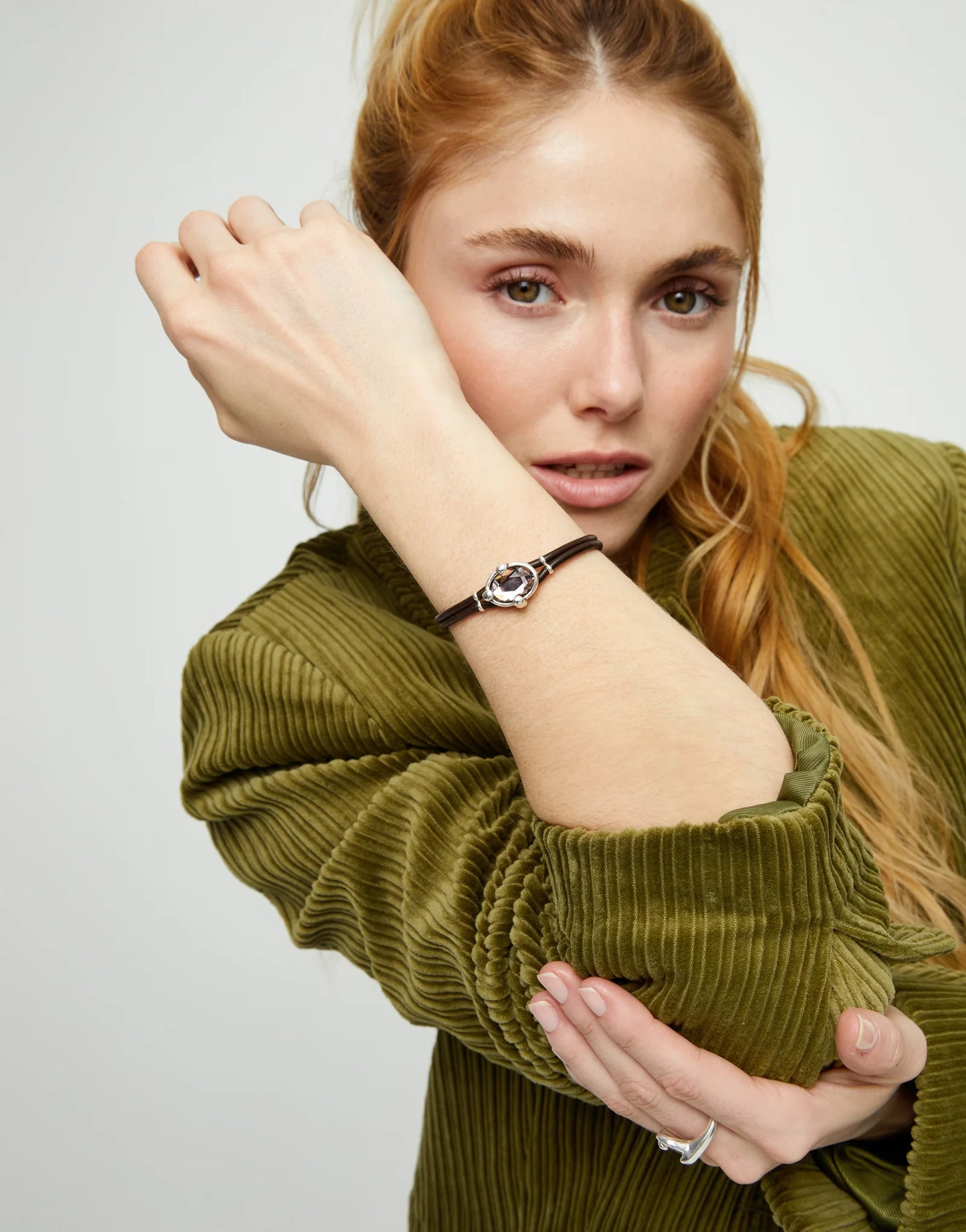 UNO de 50 Ser Deslumbrante black leather bracelet with silver trim on a model with red hair and a green jacket.