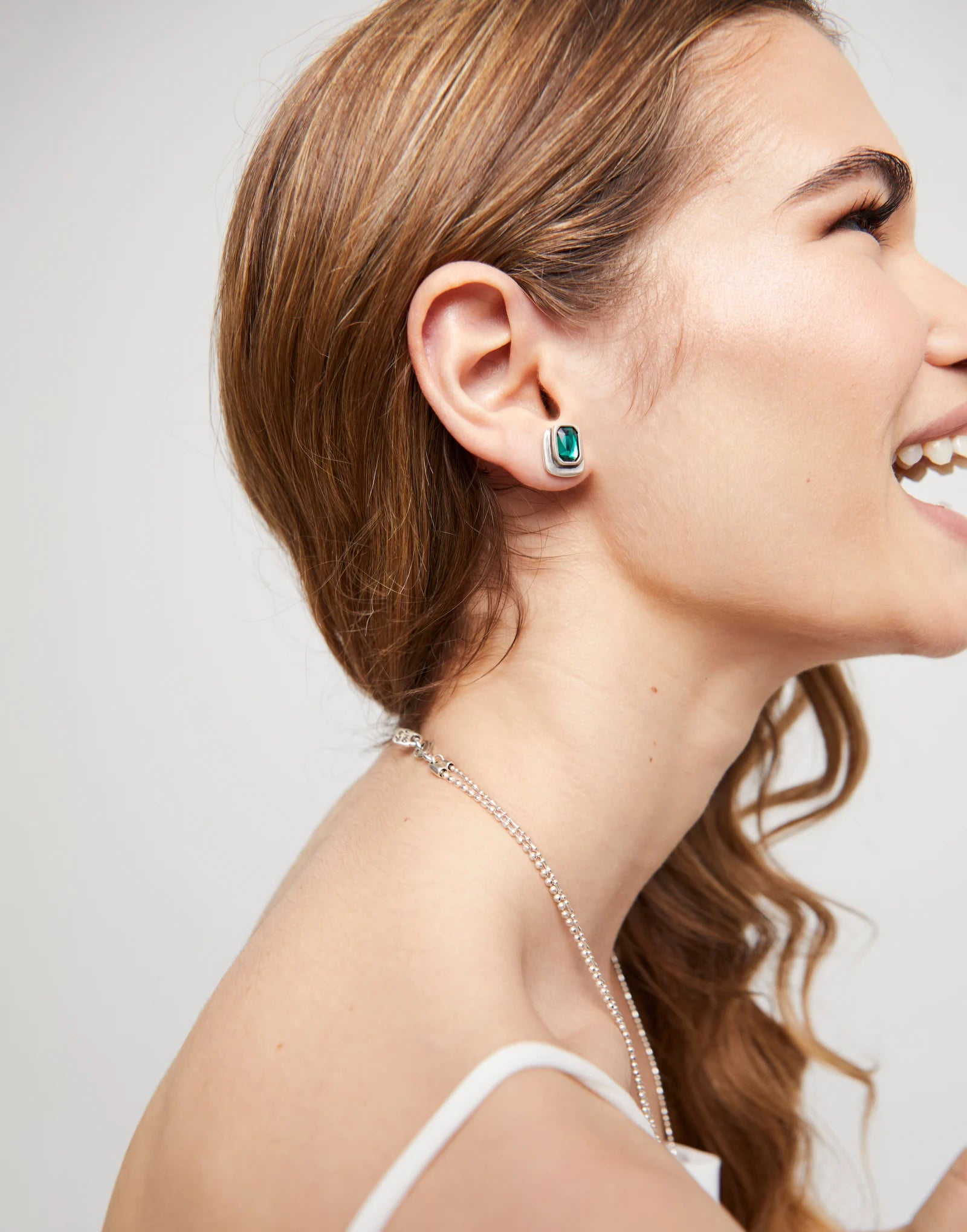 Woman wearing a silver UNOde50 silver earrings with rectangle green gemstone on a plain background