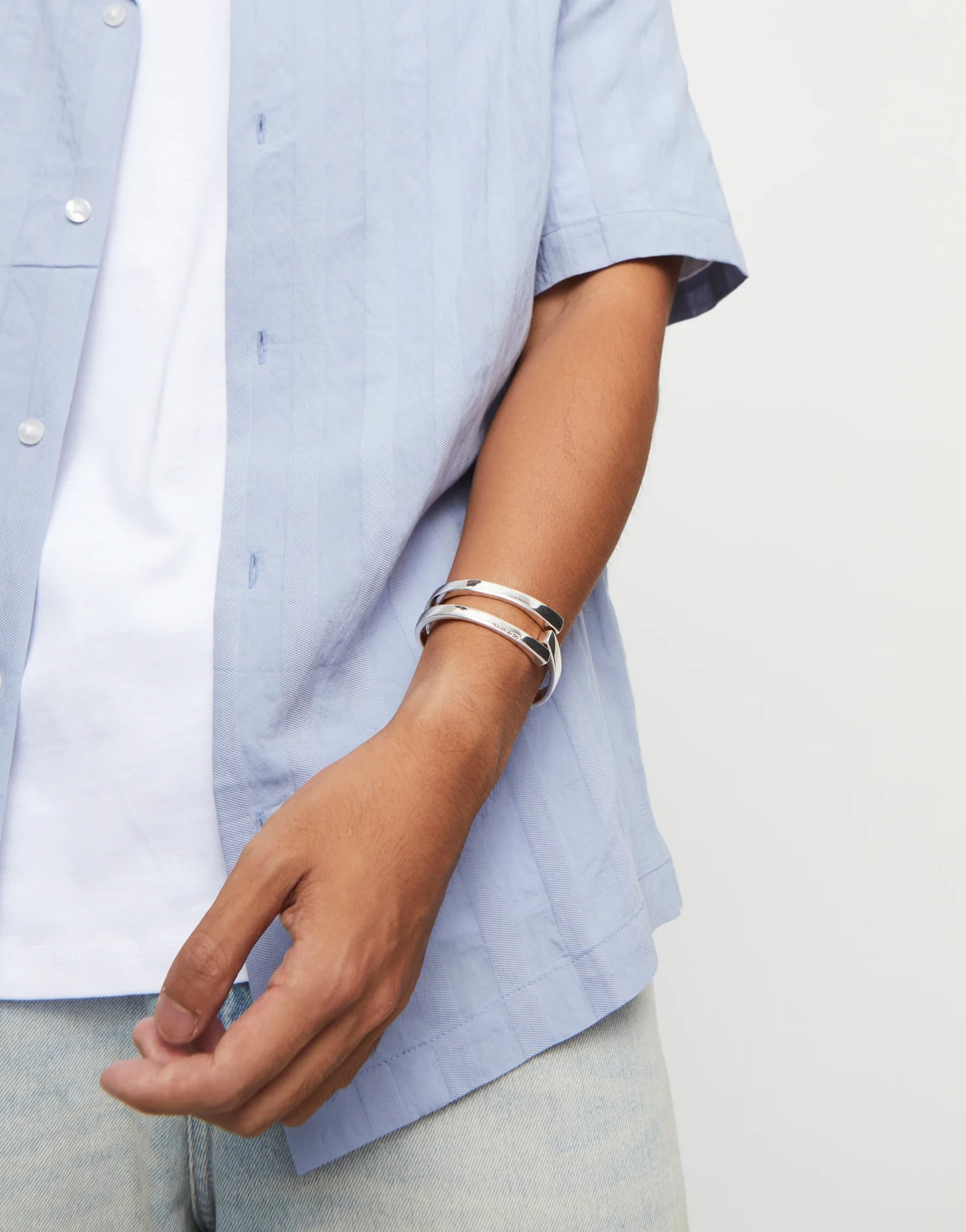 Person wearing a light blue shirt with an UNOde50 Ser Original Silver Bangle Bracelet on a plain background