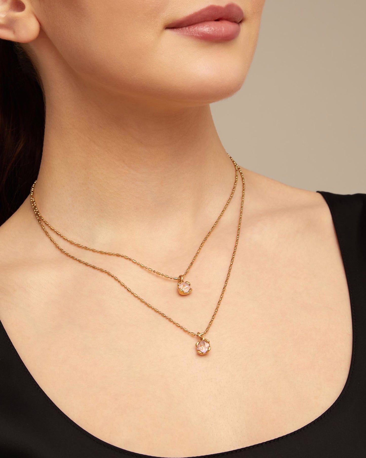 Close-up of a woman wearing an unode50 aura pink gold double necklace with pendant stones 