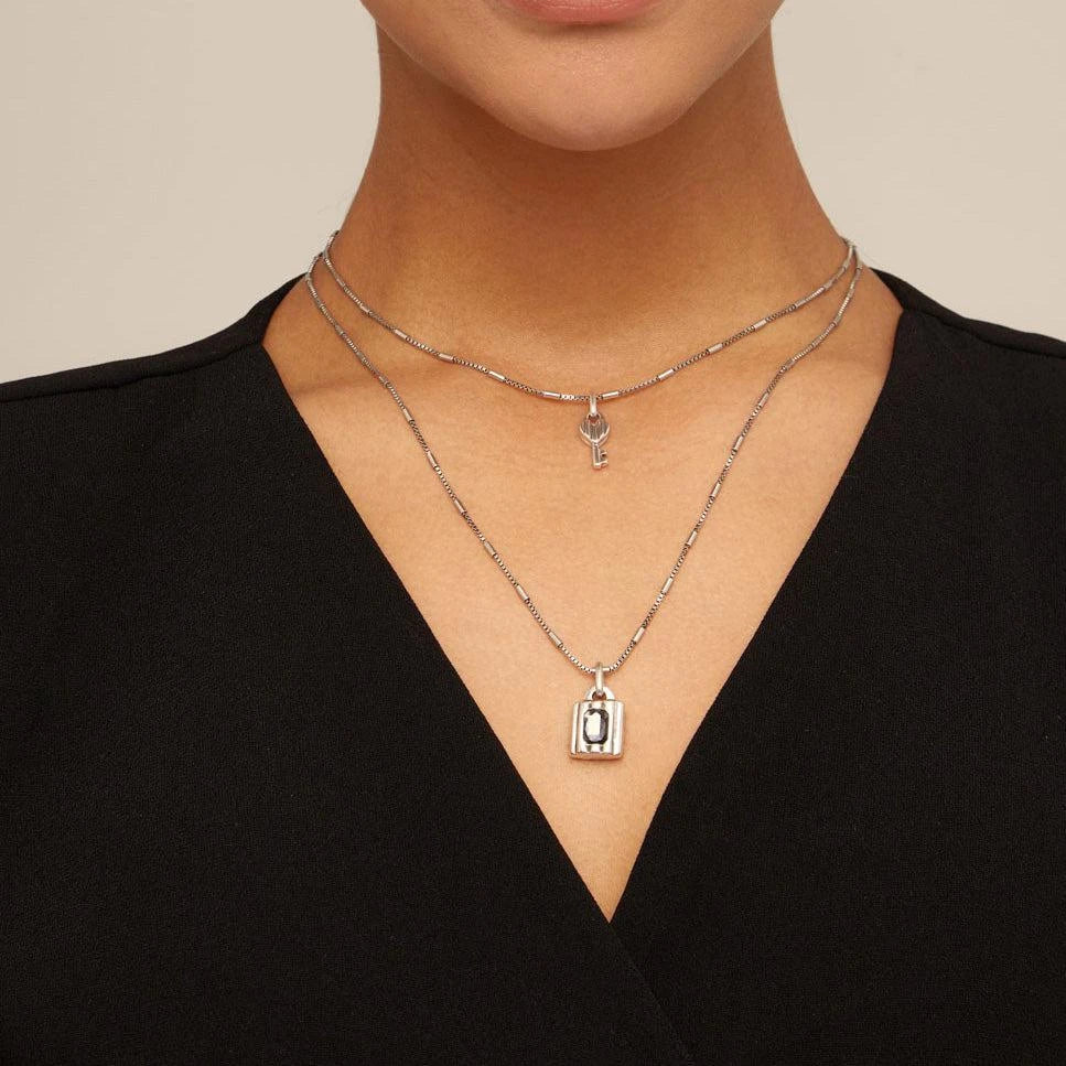 Close-up of a person wearing UNOde50 Lock Silver Double Strand Necklace with Key and Lock with Crystal on a neutral background
