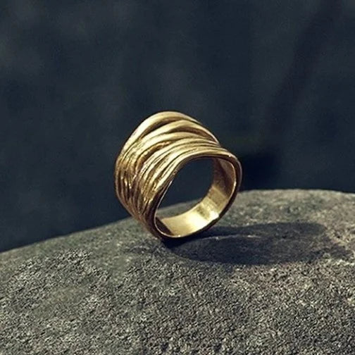 UNOde50 Nihiwatu Beach Gold Stacked Ring with wavy design on a dark stone surface