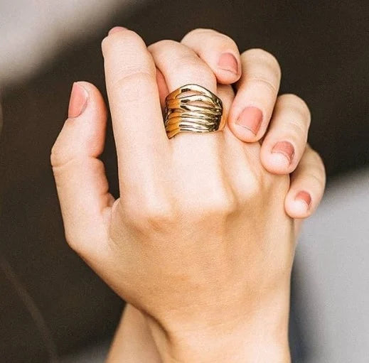 Hand wearing a UNOde50 Nihiwatu Beach Gold Stacked Ring with a textured design on a neutral background