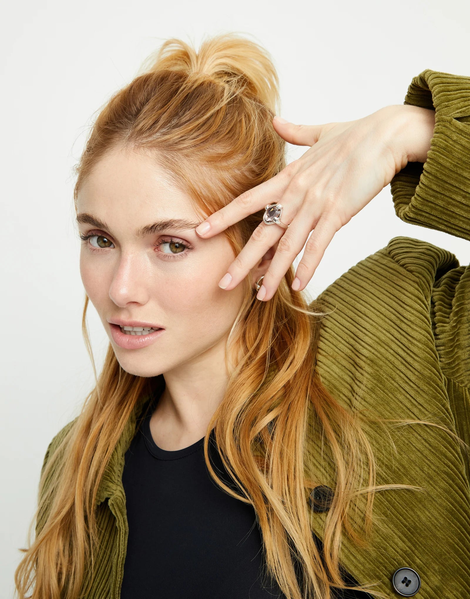 Woman with styled hair and a green jacket wearing an UNOde50 Ser Deslumbrante Silver Ring with Pink Oval Crystal against a white background