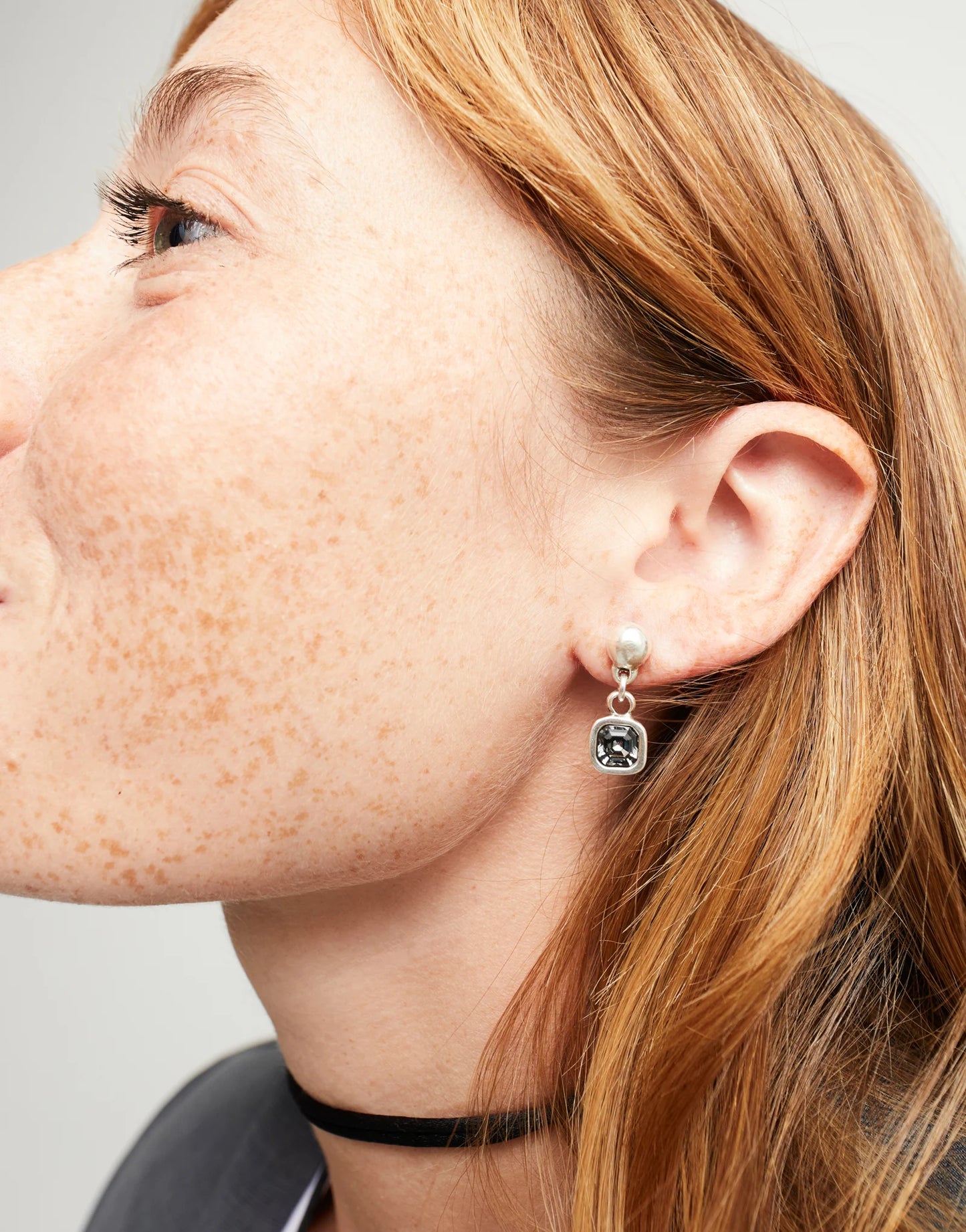Close-up of a person wearing a silver UNOde50 Ser Expresiva drop earring with a black stone on a neutral background