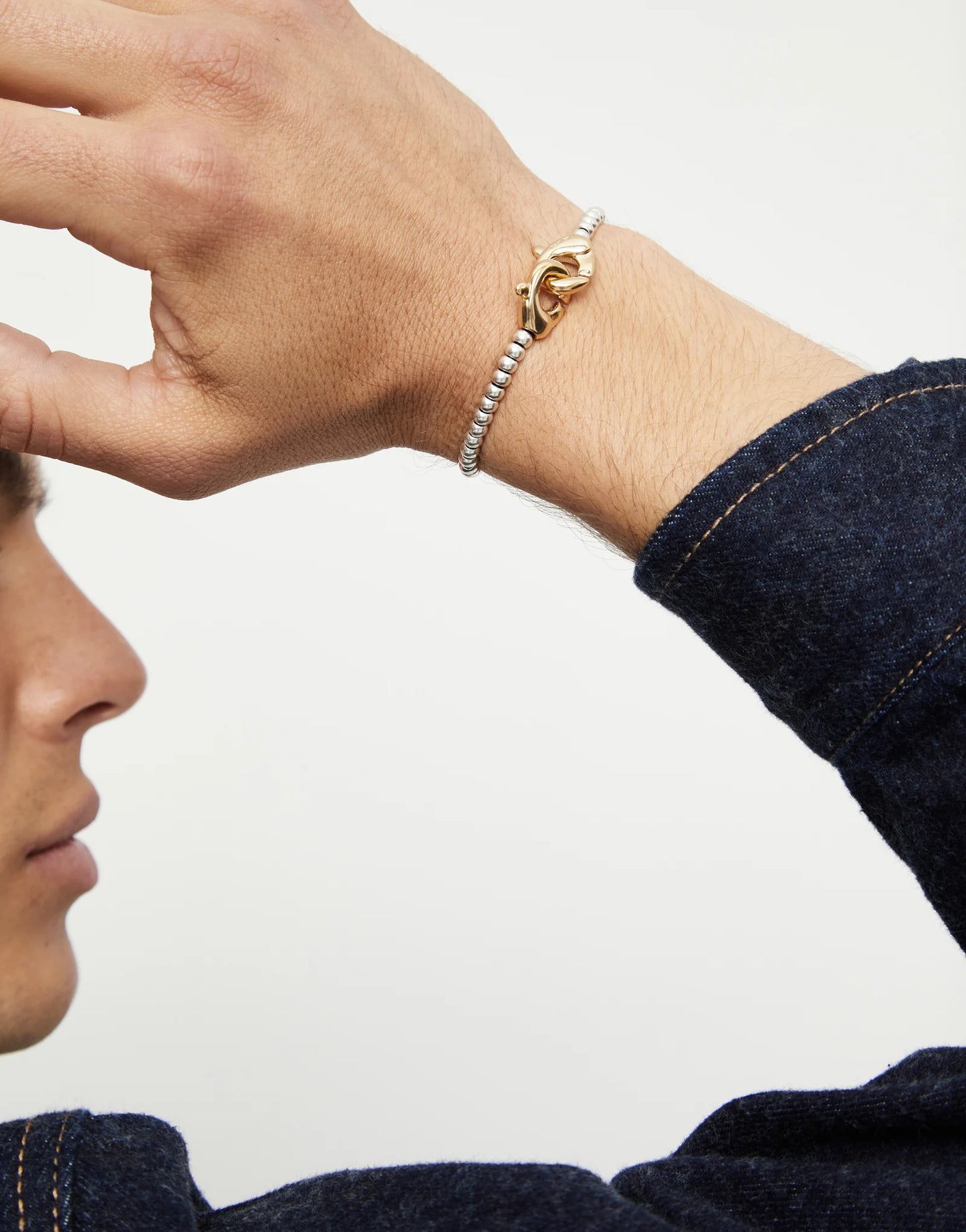 A persons wrist showing an UNOde50 Ser Inseparable silver bracelet with Gold clasp on white background