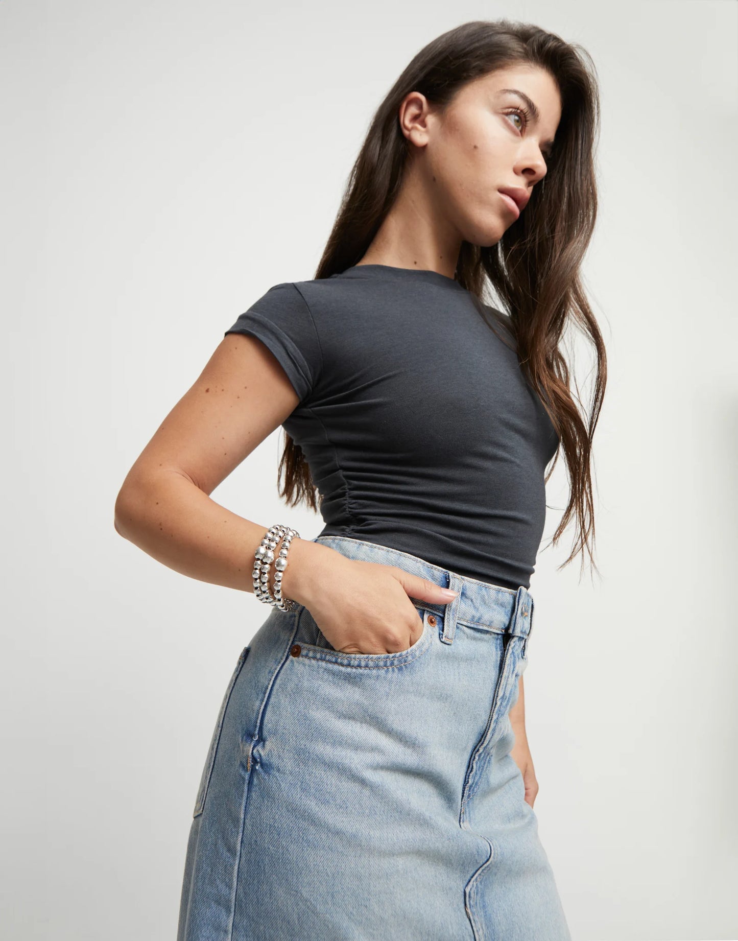 Woman wearing a dark gray t-shirt and light blue jeans wearing an  UNOde50 silver beaded 3 strand bracelet against a plain background