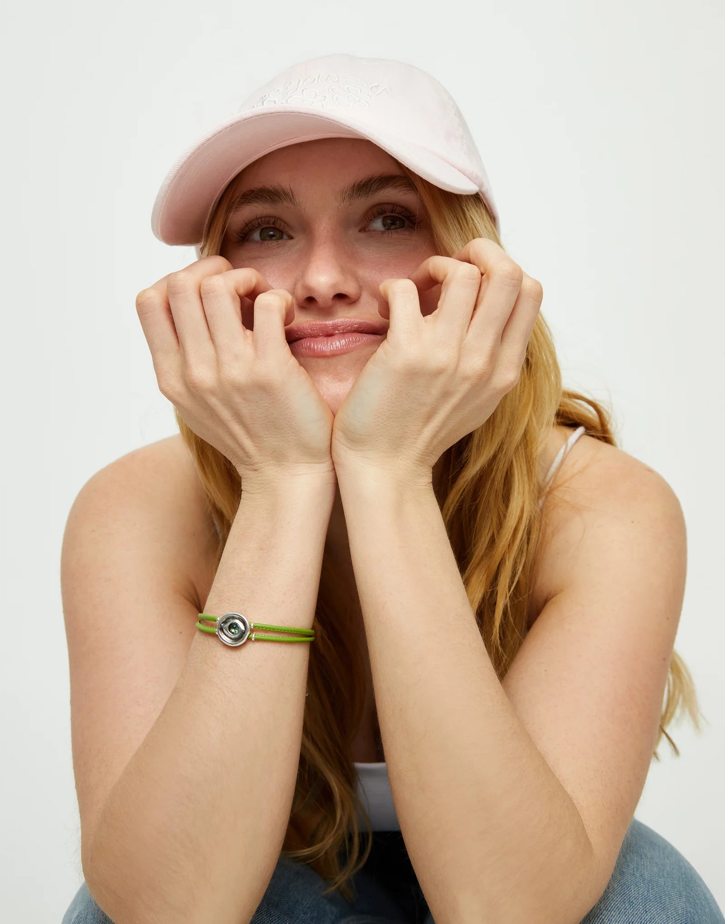 Woman wearing a pink cap and an SALE UNOde50 Ser Intuitiva Double Green Leather Bracelet with Silver and Green Crystal on a white background