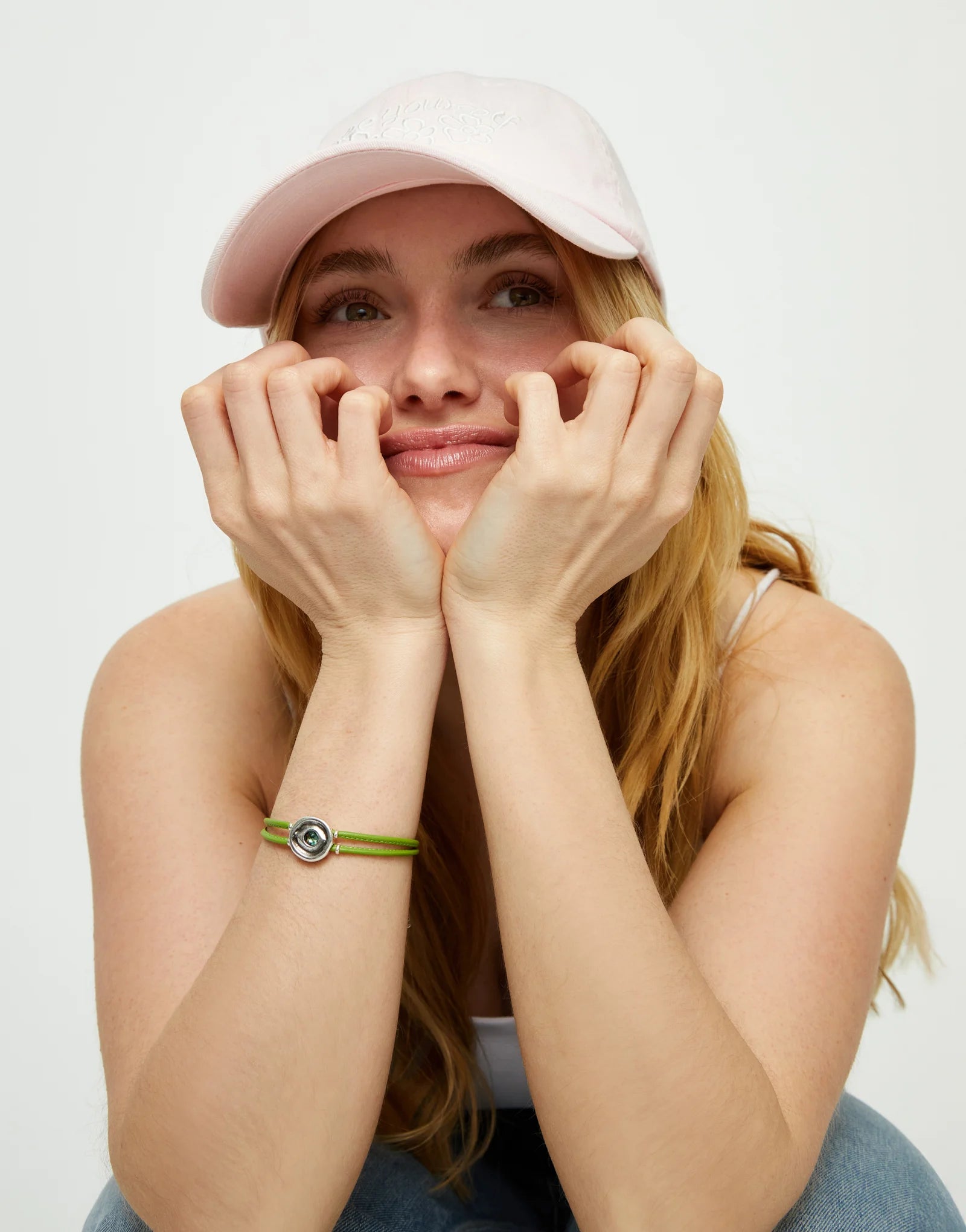 Woman wearing a pink cap and an SALE UNOde50 Ser Intuitiva Double Green Leather Bracelet with Silver and Green Crystal on a white background