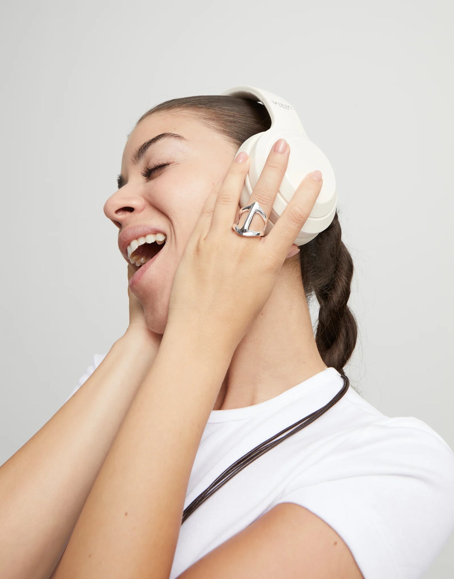 Woman wearing white headphones and an UNOde50 Ser Majestuosa Manta-Ray Shaped Silver Ring and laughing against a plain background