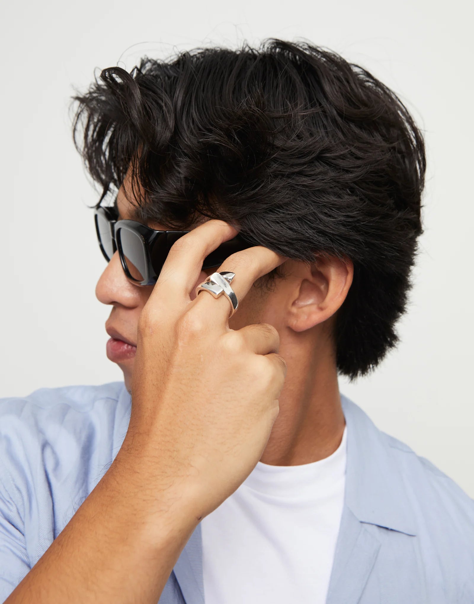 Man adjusting sunglasses with dark hair and an UNOde50 Ser Original Silver Ring with Curved Lines with a plain background