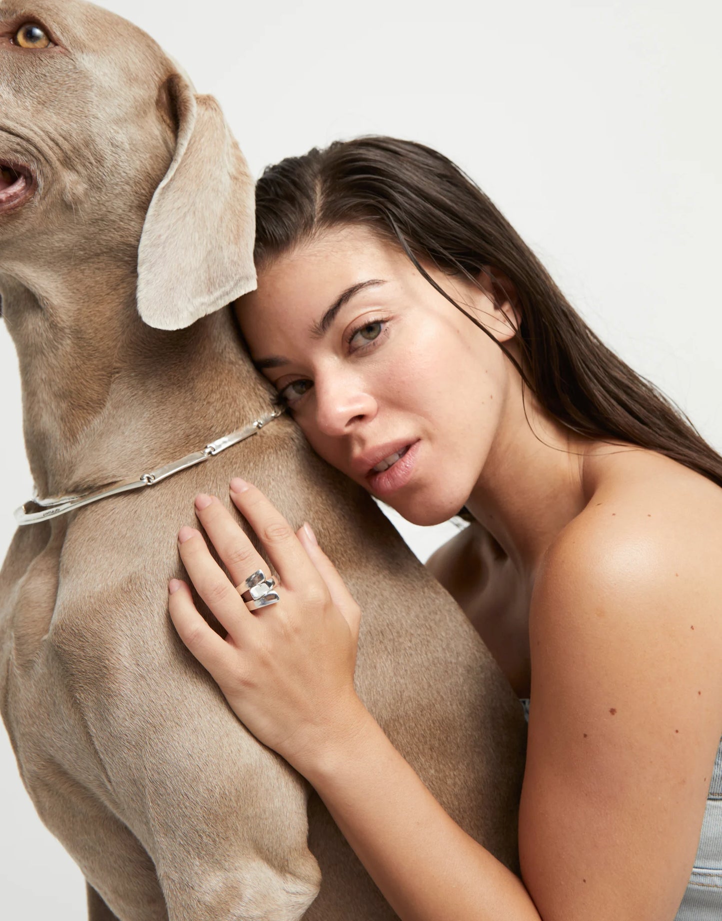 Woman hugging a large dog wearing an UNOde50 Ser Original Silver Ring with Curved Lines on a plain background