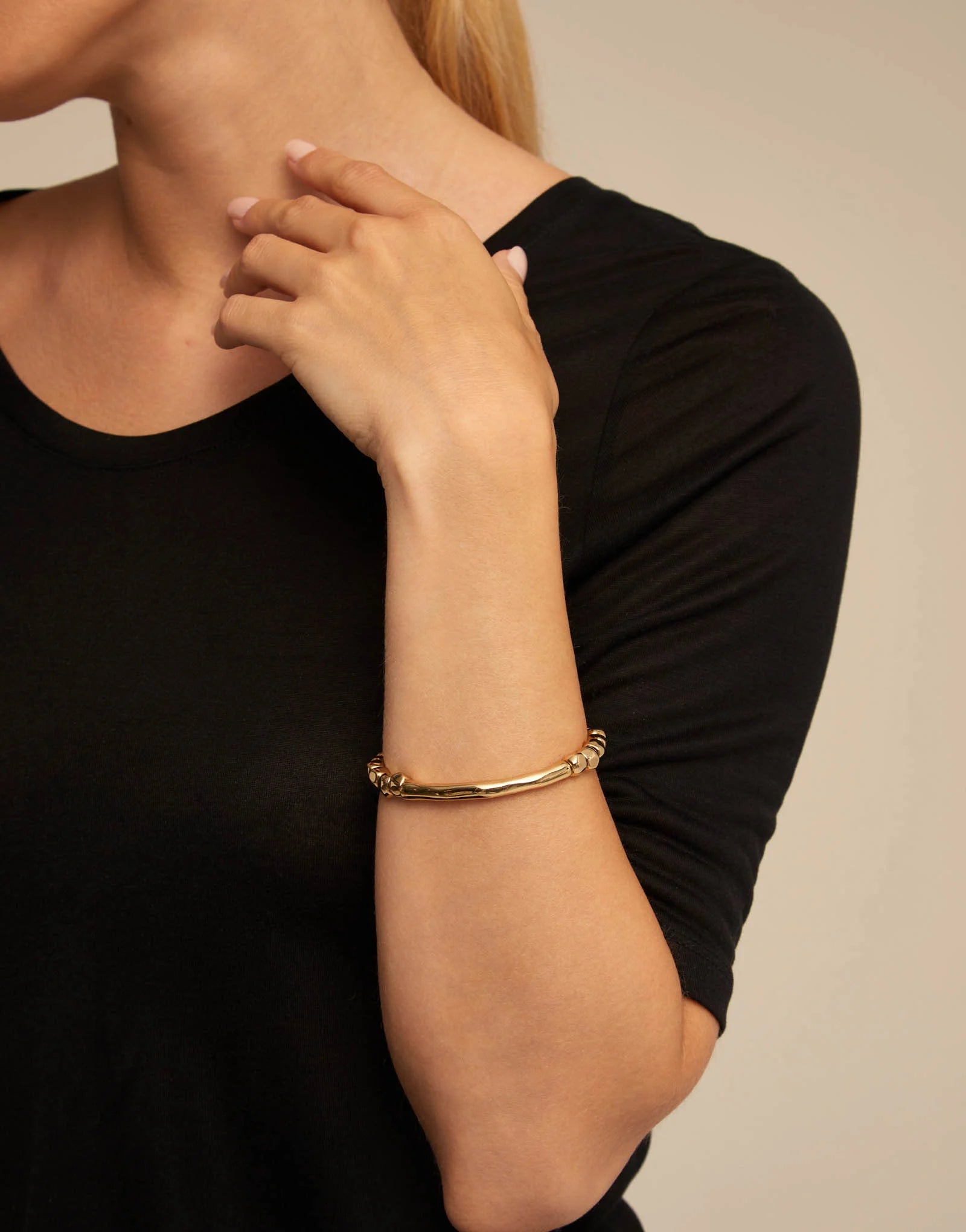 Woman wearing a black shirt and an UNOde50 Trabel Gold Beaded Stretch Bracelet with Tubular Accent