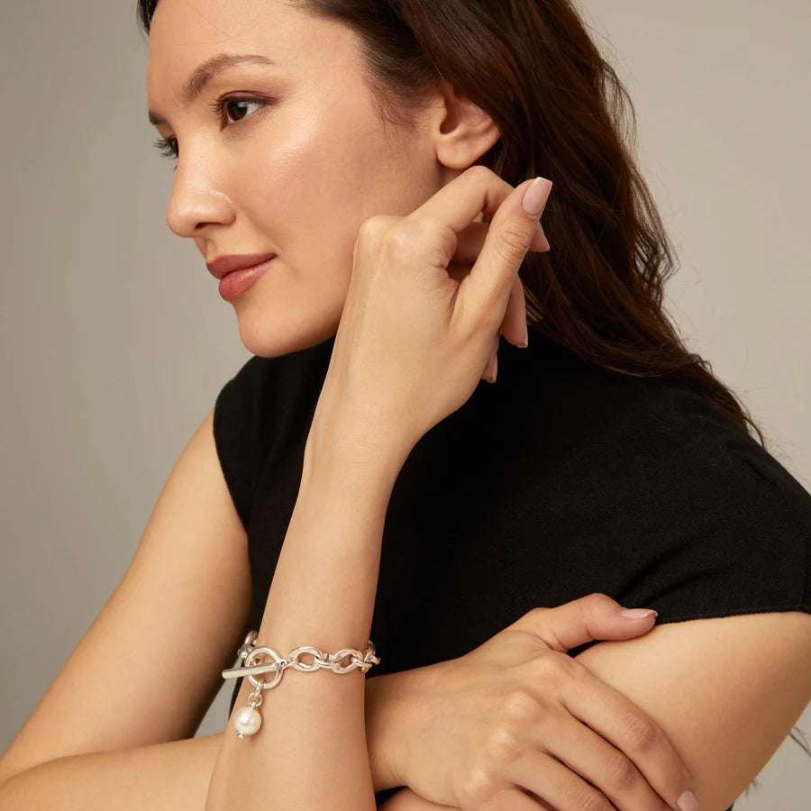 Woman in a black dress wearing an UNOde50 YOLO Silver link bracelet with a pearl charm with a circle and bar clasp