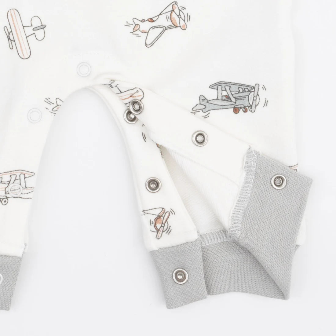 Close-up of an angel dear vintage pilots  baby romper or long-sleeve top in white fabric with a light gray and orange airplane print, featuring gray ribbed cuffs and snap closures.