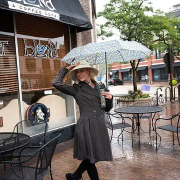 Woman holding a Vinrella In bloom bottle umbrella in front of a coffee shop with outdoor seating.