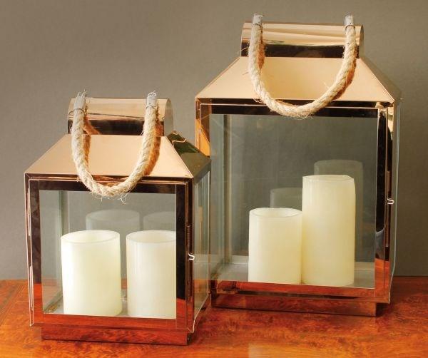 Two metallic copper lanterns with candles inside on a wooden surface.