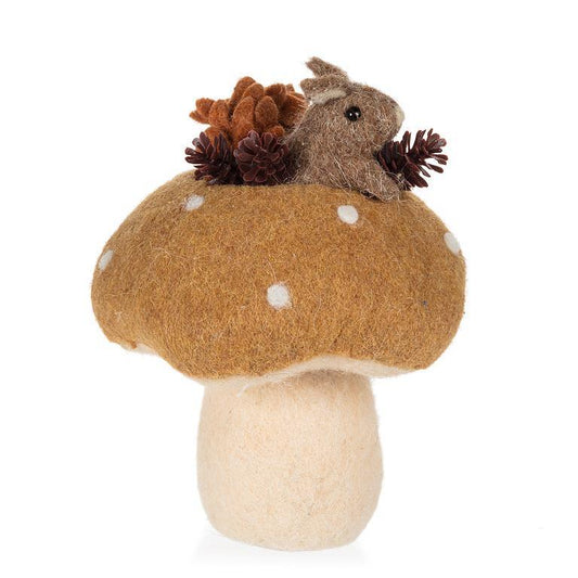 A felt mushroom decoration with a brown cap, white polka dots, a cream stem, and a small brown squirrel sitting on top holding pinecones, photographed on a white background.