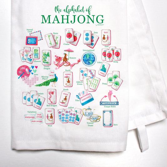 A white kitchen towel featuring a colorful printed graphic of mahjong cards and tiles, with the text 'the alphabet of MAHJONG' in green at the top.