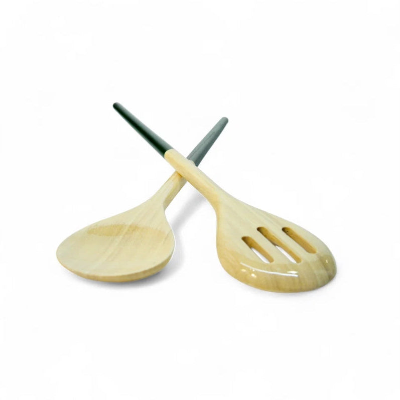 Two wooden salad serving spoons crossed over each other on a plain white background. One spoon has a smooth natural wood finish, and the other has three slots in the bowl, both with dark green handles.