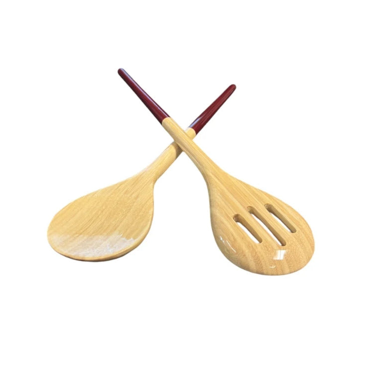 Two wooden salad serving spoons crossed over each other on a plain white background. One spoon has a smooth natural wood finish, and the other has three slots in the bowl, both with red handles.