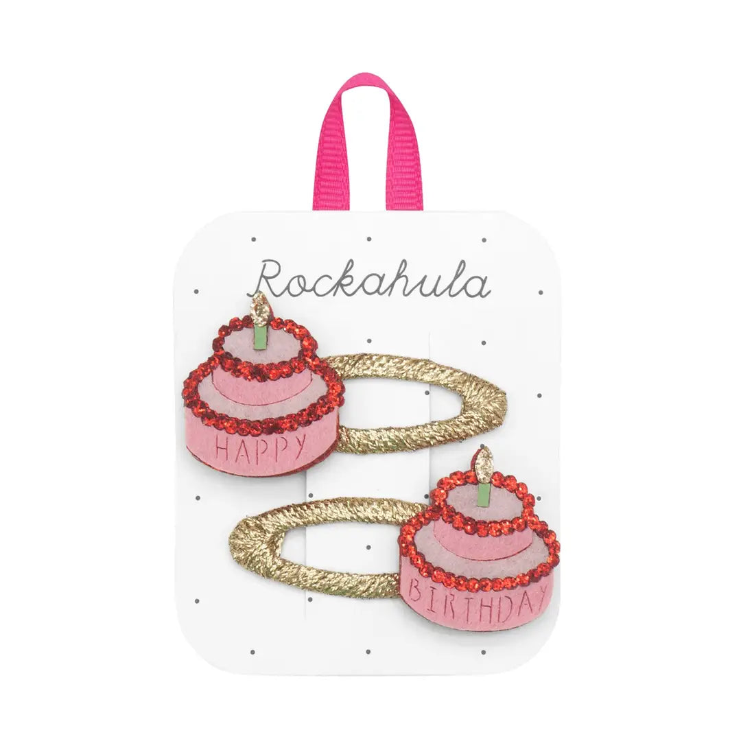 Two pink birthday cake hair clips with gold ribbons on a white card with 'Rockahula' branding.