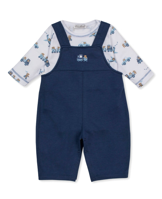 A baby boy's short-sleeve overall romper in navy blue, featuring a white long-sleeve shirt underneath with a blue and tan bears in transportation vehicles pattern.
