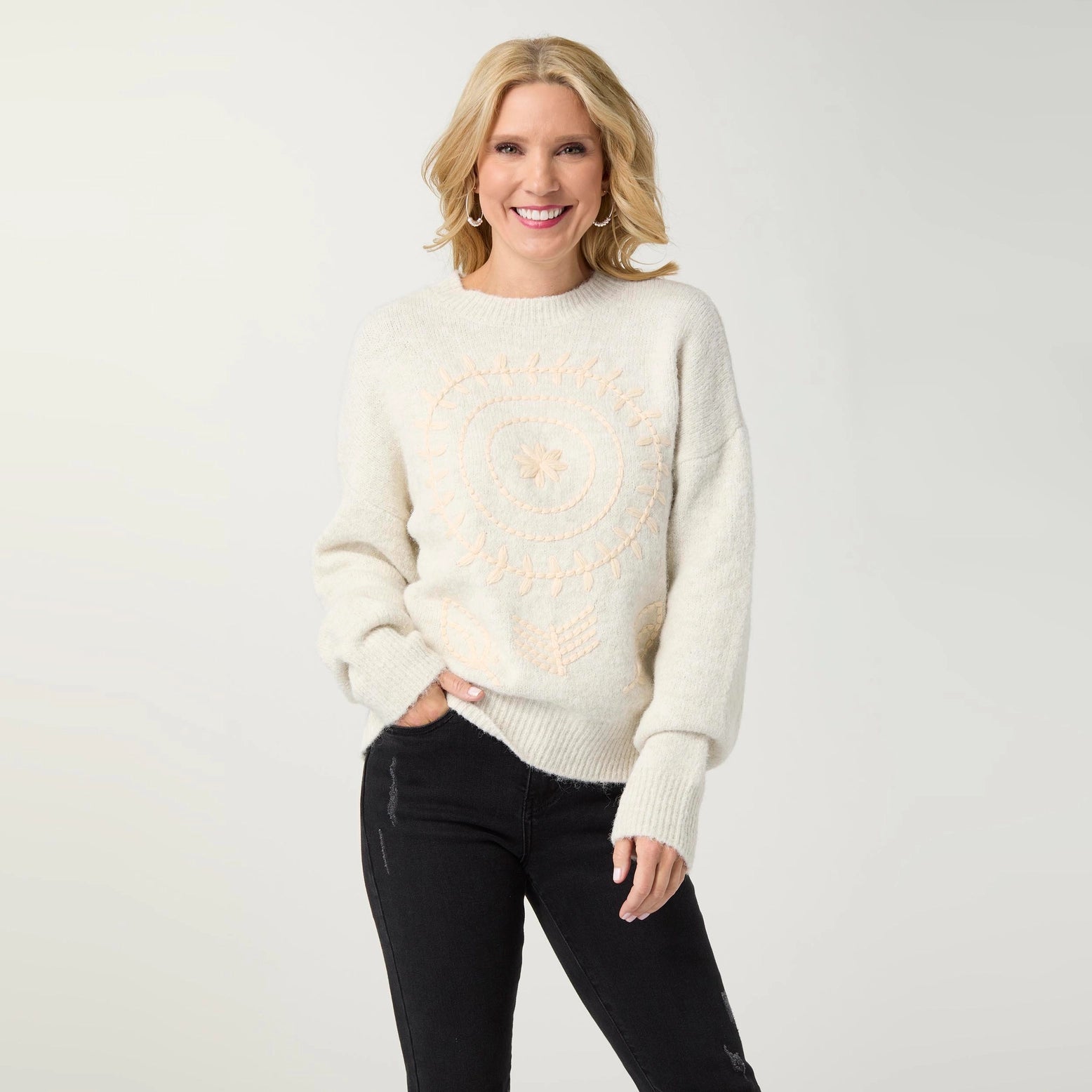 A woman wearing a cream-colored fuzzy knit sweater with a peach circular graphic on the front.