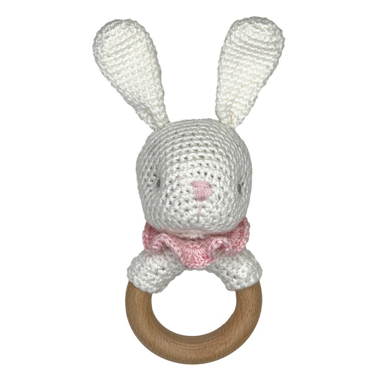 A crocheted bunny teething ring toy. The bunny is made from white textured yarn with a small pink stitched nose and a pink ruffled collar, attached to a natural wooden ring.