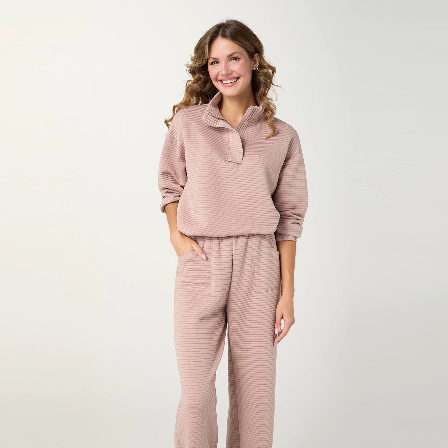 A woman modeling a matching two-piece loungewear set in a dusty rose pink color with fine horizontal stripes. The set includes a long-sleeve quarter-placket top and matching wide-leg pants.