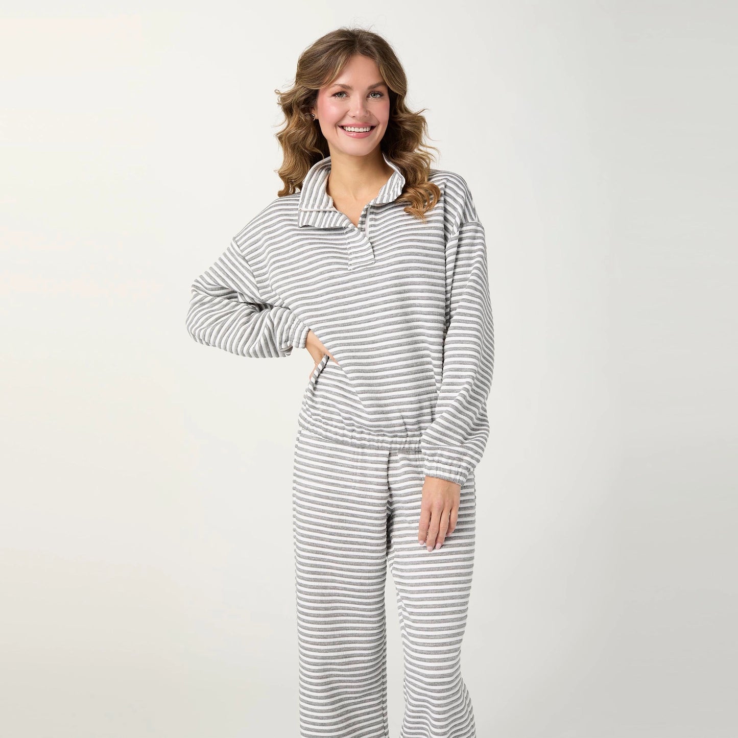 A woman modeling a matching two-piece loungewear set with a long-sleeve collared top and wide-leg pants, both featuring thin gray and white horizontal stripes.