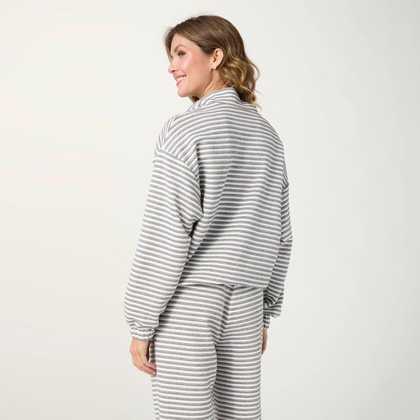 A woman wearing a matching gray and white striped lounge set, shown from a side-back angle against a plain light gray studio background.