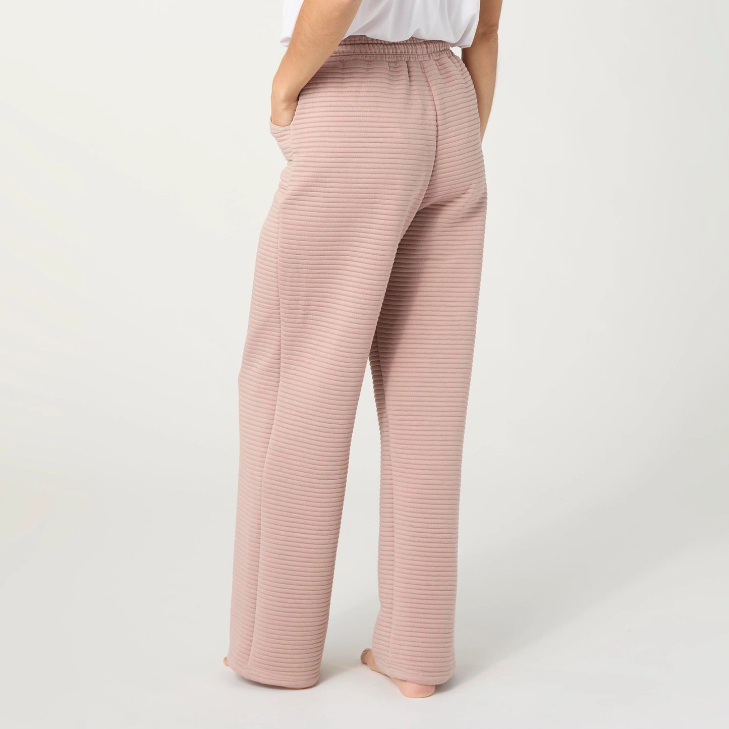 A person shown from the back wearing wide-leg trousers in a dusty pink color with subtle horizontal stripes, paired with a white top, against a light gray studio background.