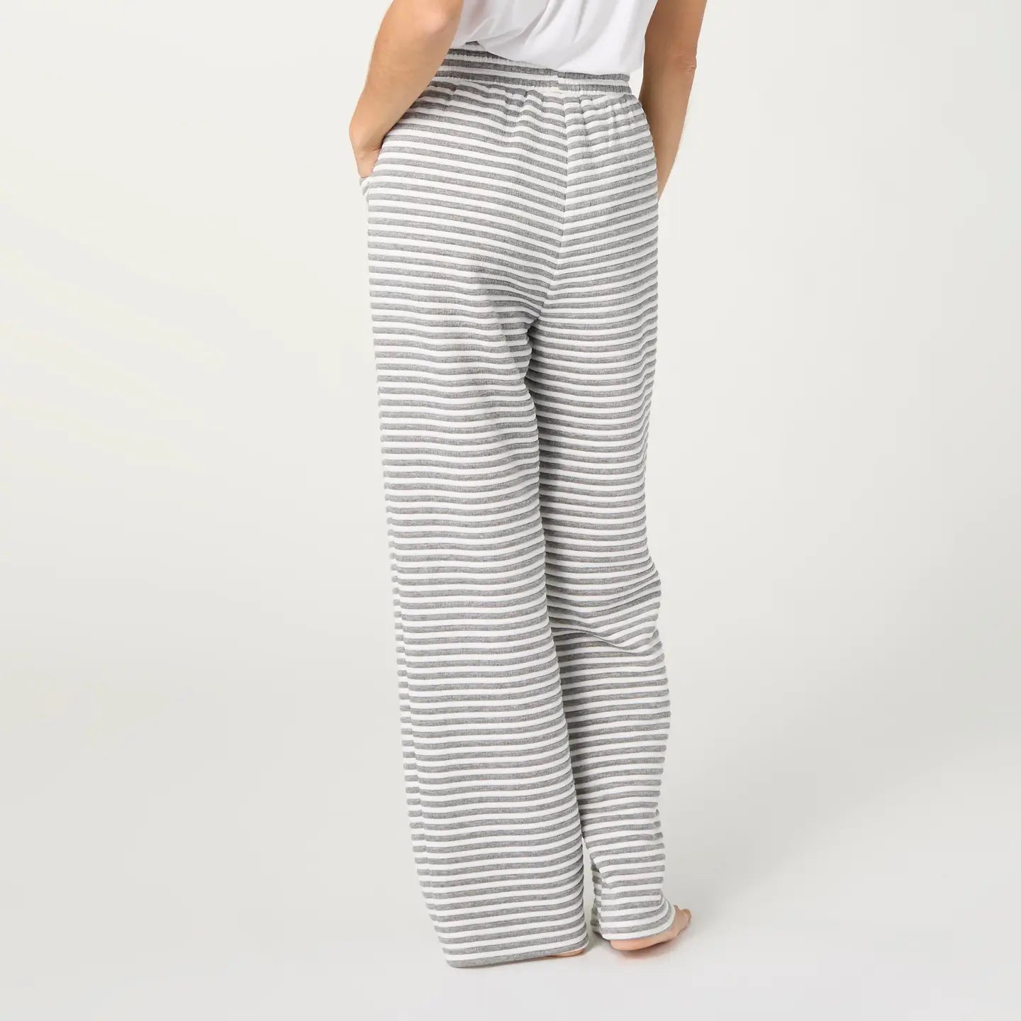 A person shown from the back wearing loose, wide-leg pants with thin horizontal gray and white stripes, standing against a plain light gray studio background.