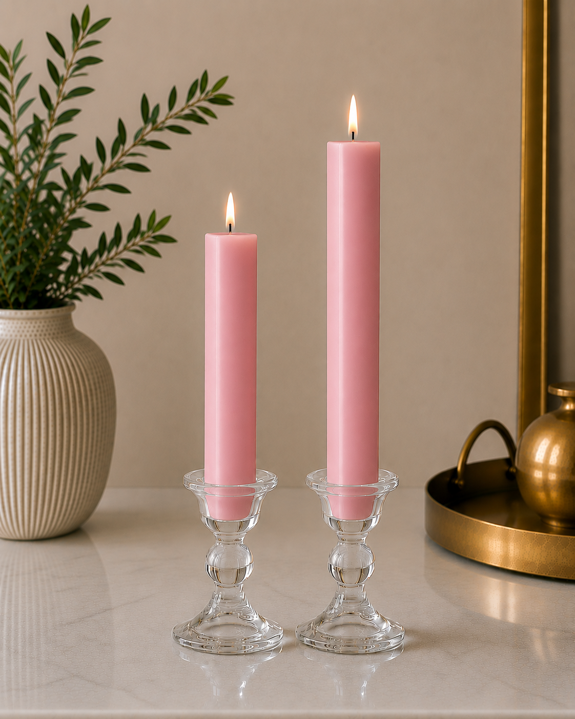 Two #75 Silky pink 8" and 12" square taper pillar beeswax candles by Dadant  in clear glass candlesticks on a marble surface, with a potted plant on the left and a brass tray on the right.