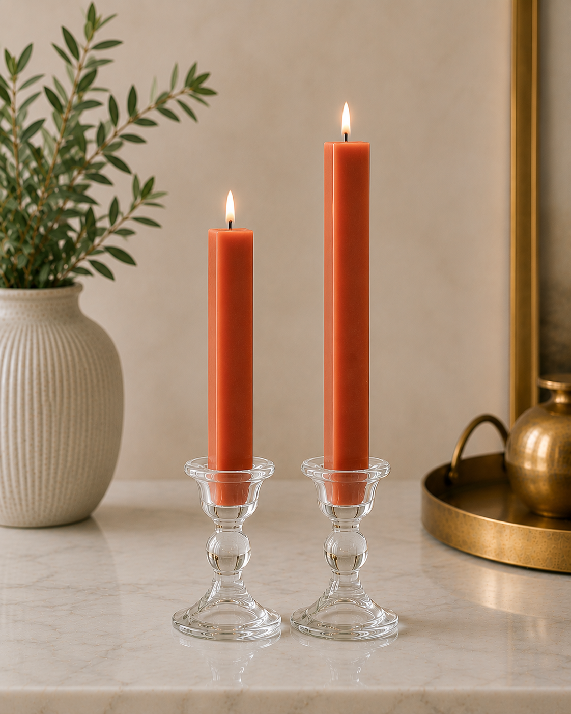 Two #08 Terra Cotta 8" and 12" square taper pillar beeswax candles by Dadant  in clear glass candlesticks on a marble surface, with a potted plant on the left and a brass tray on the right.